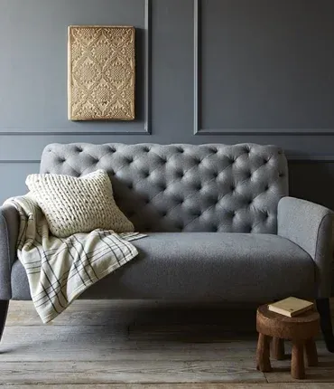 A stylish gray tufted sofa with a decorative pillow and a cozy blanket