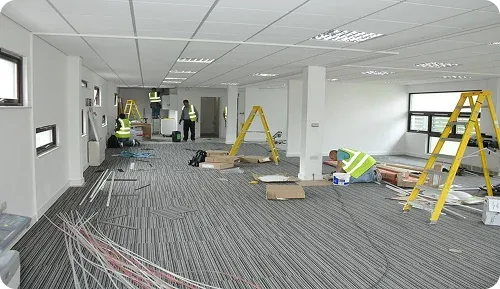 Construction workers in safety vests work in an unfinished office space with ladders