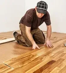 A man kneels on the floor, installing wooden planks in a room