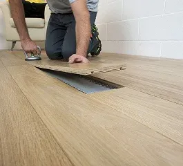 A person fitting a wooden floor panel over a duct