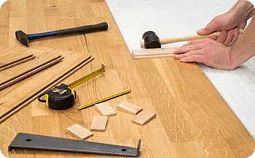 A person's hands use a mallet to secure wood pieces on a wooden surface