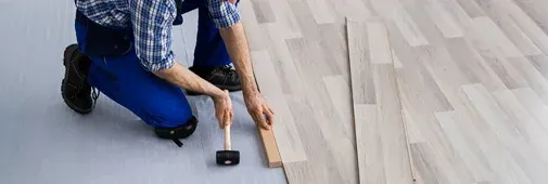 A worker in a checked shirt and blue pants kneels on a floor