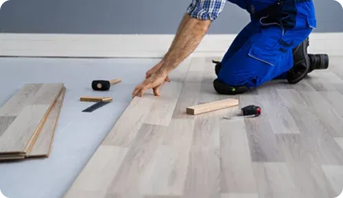 Person installing flooring, tools nearby, kneeling position