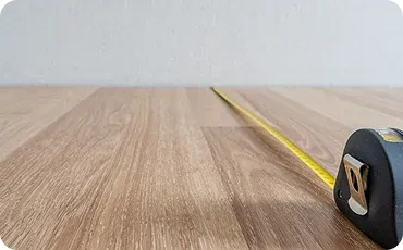 Tape measure on wooden floor, wall in background.